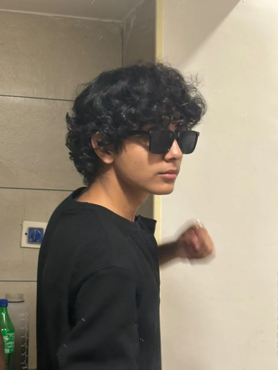 Aayan in sunglasses and a black knit sweater, side profile