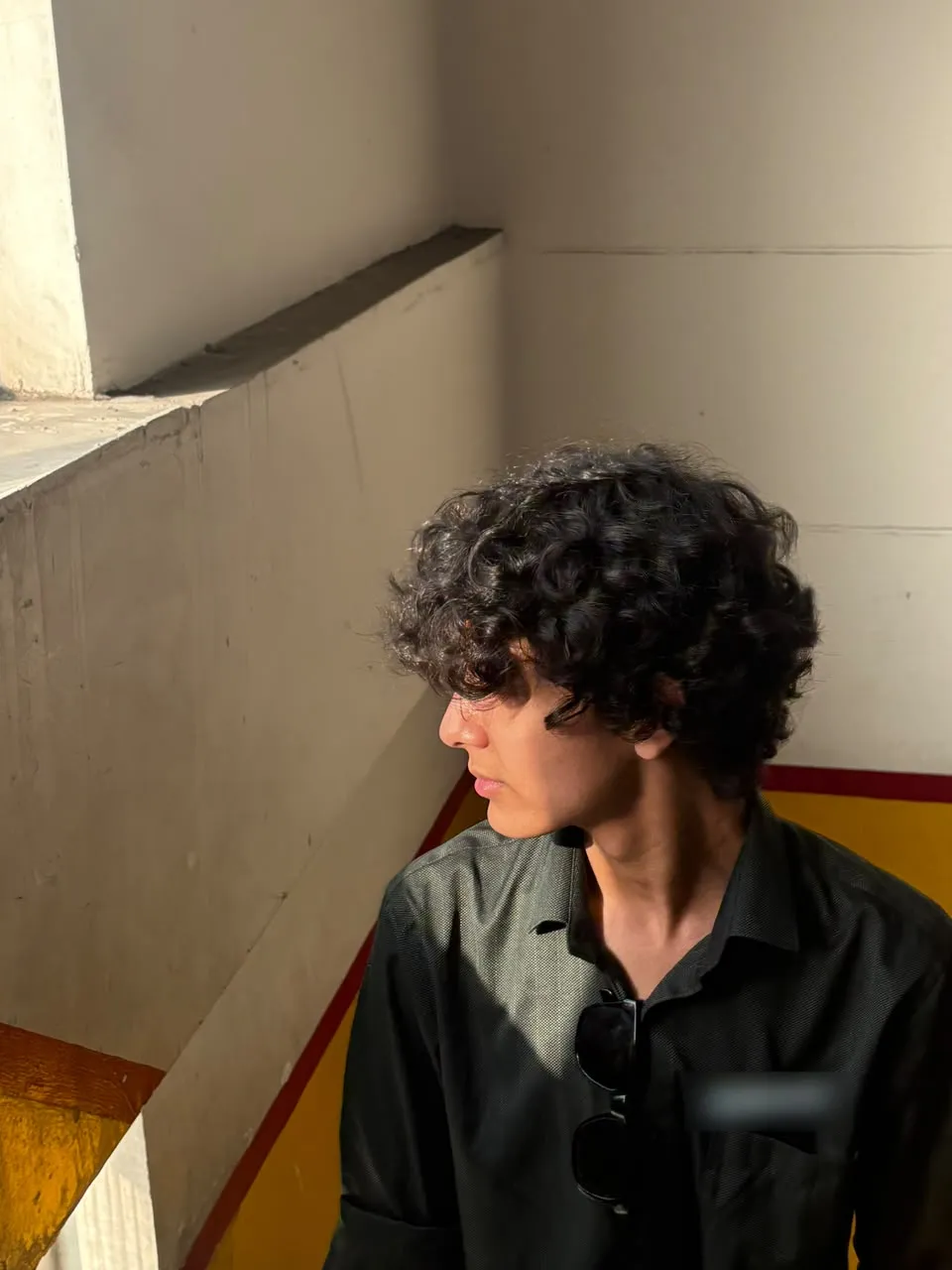 Aayan in a black shirt on a sunlit stairwell, looking away