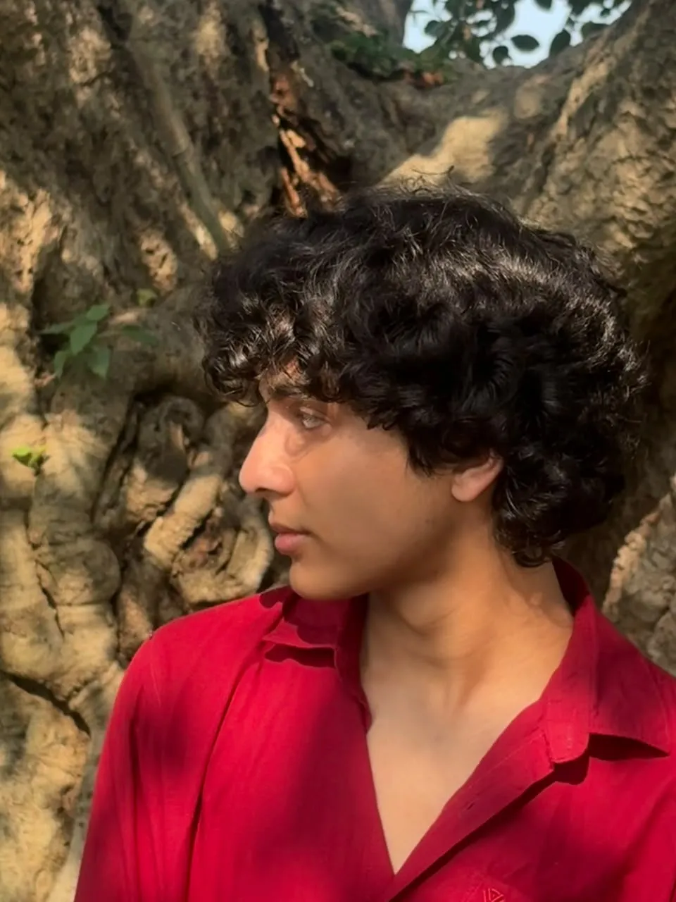 Close side profile of Aayan in a red shirt against a tree